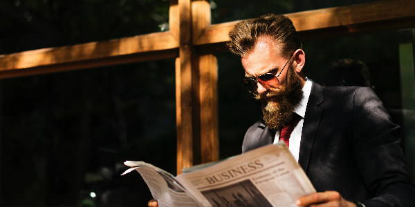 Corporate man reads the business pages outside a coffee shop, symbolizing how people are interested in reading about employee benefits and staff retention