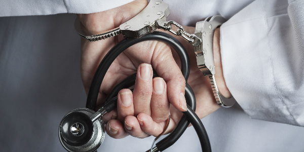Close up shot of a doctors hands, clutching a stethoscope, handcuffed, relaying the idea that health care system fraud is a serious challenge