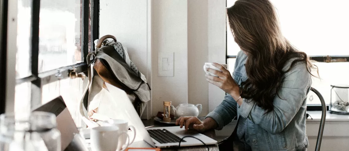 a businesswoman sits at a hot desk with a laptop and a coffee, symbolizing flexible work arrangements and the need to consider part time employee benefits