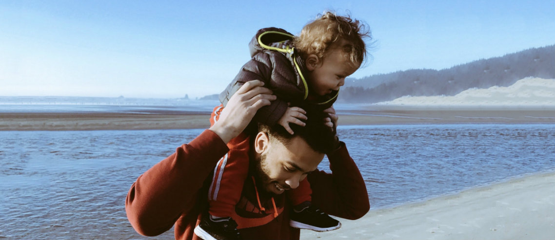 a child rides his father's shoulders on the beach signifying the need for companies to consider employee life insurance to protect loved ones