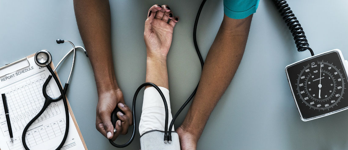 birds eye view of a health professional takes the blood pressure of a patient as a covered employee medical insurance benefit