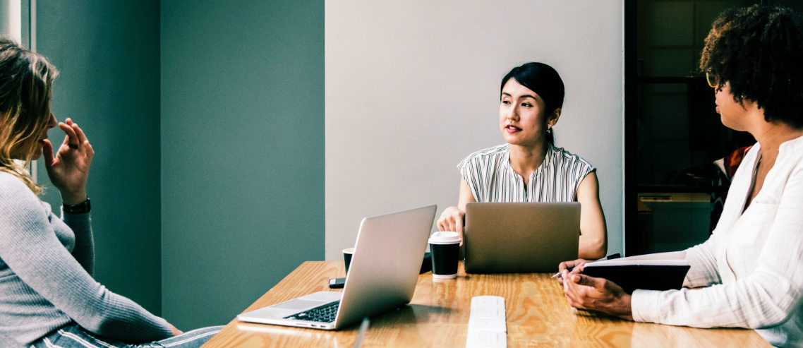 a woman sits at the head of a meeting table with two colleagues, discussing the need for healthcare for small businesses
