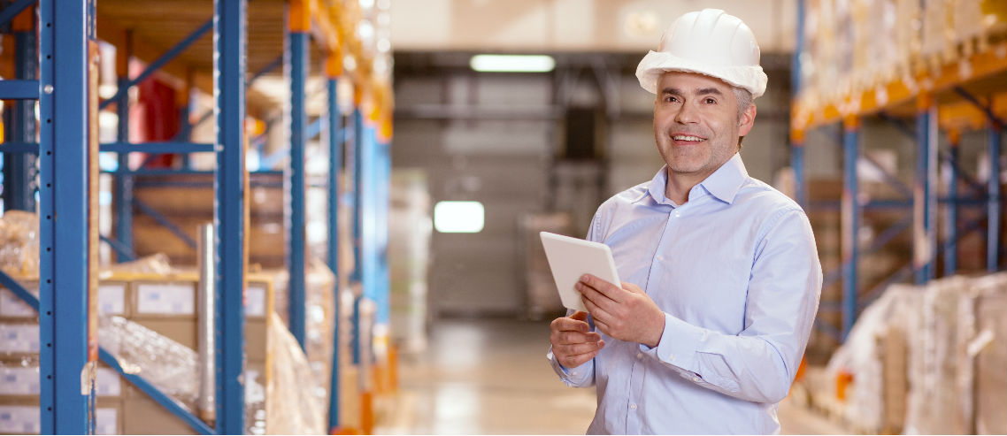 a gen x male manager stands with a hardhat in a warehouse, overseeing stock and inventory, symbolizing the need to understand the management benefits needs of gen x employees