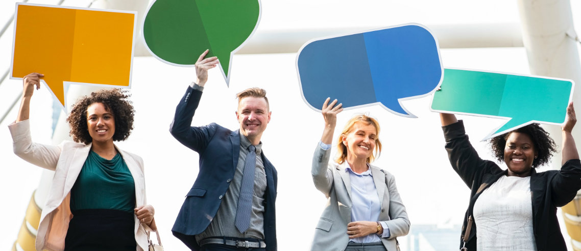 a diverse group of professionally dressed employees hold up feedback speech bubbles symbolizing the importance of understanding employee engagement with your employee benefits solutions