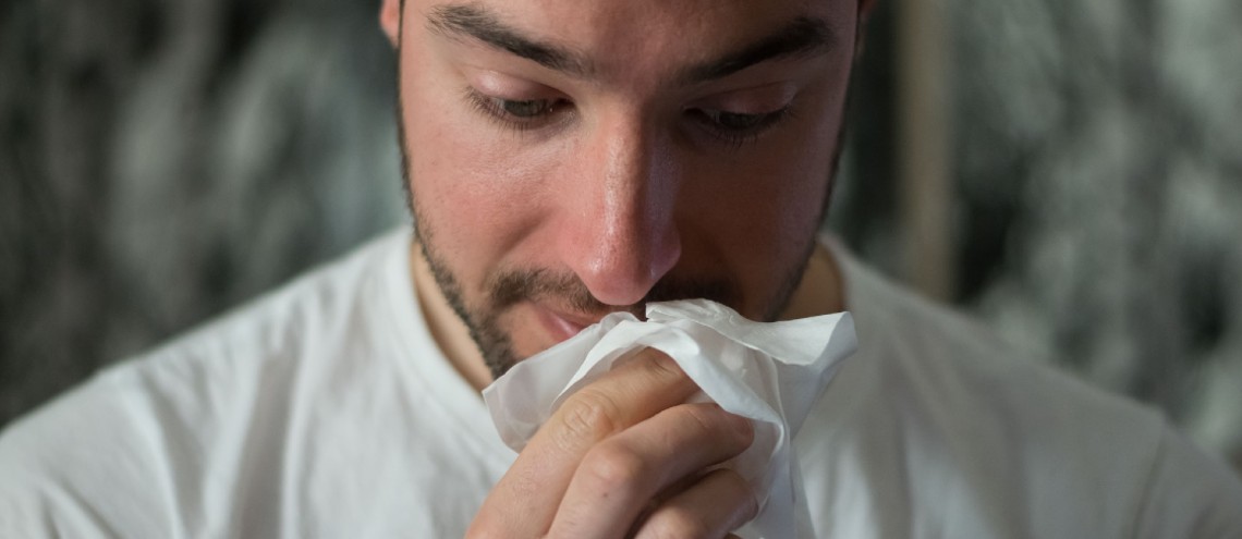 Man with facial hair using tissue to wipe his nose