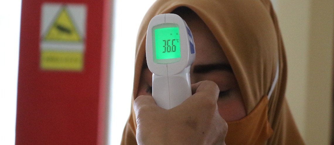 Handheld temperature reader being used on a woman in a hijab