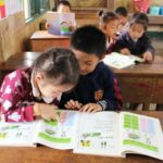 two students compare books at their desks in a room to read and pacific prime built school in laos