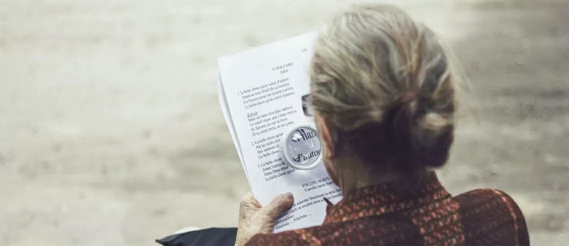 Old woman with Alzheimer's disease reading with a magnifying glass.