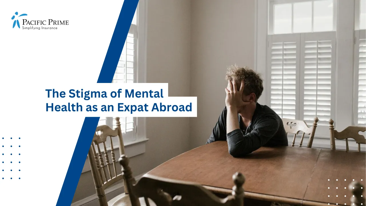 Image of Man Leaning Forward With Arms Resting On Wooden Table with text overlay of "The Stigma of Mental Health as an Expat Abroad"