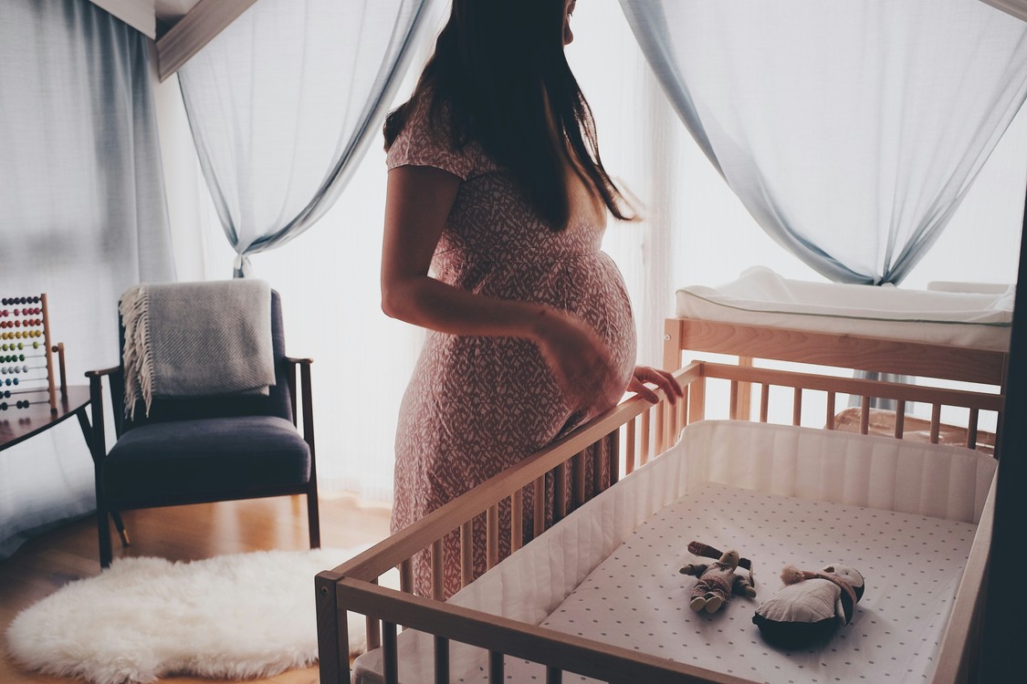 Pregnant Woman By Crib In White Dress