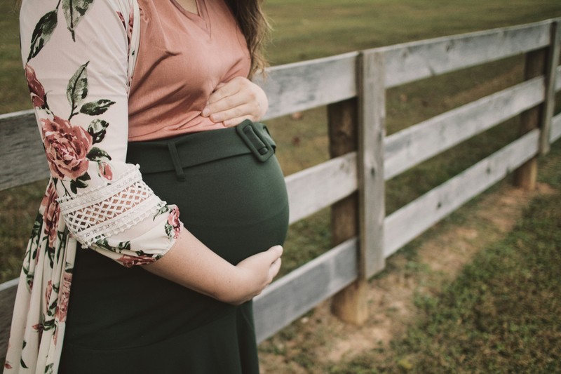 Pregnant Woman Standing By A Fence