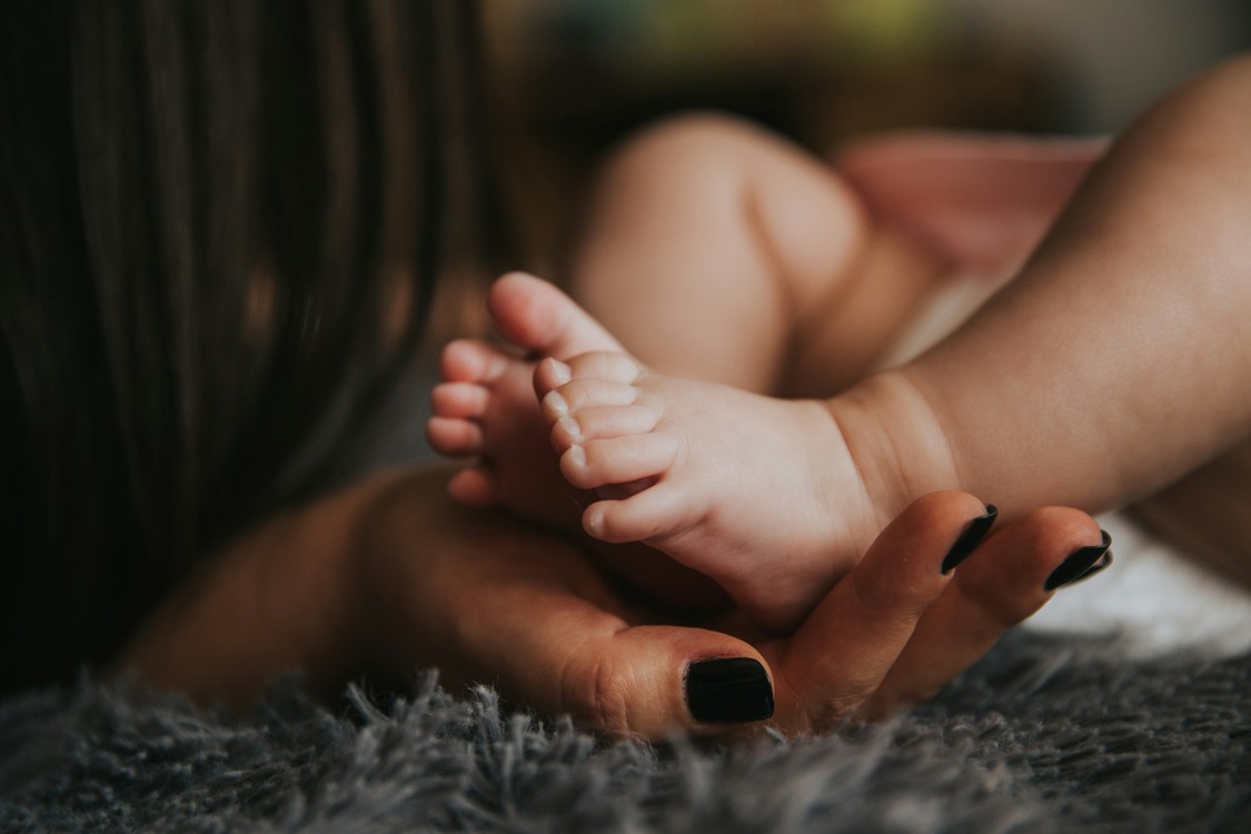 Woman's Hand Holding Infant's Feet On Gray Blanket